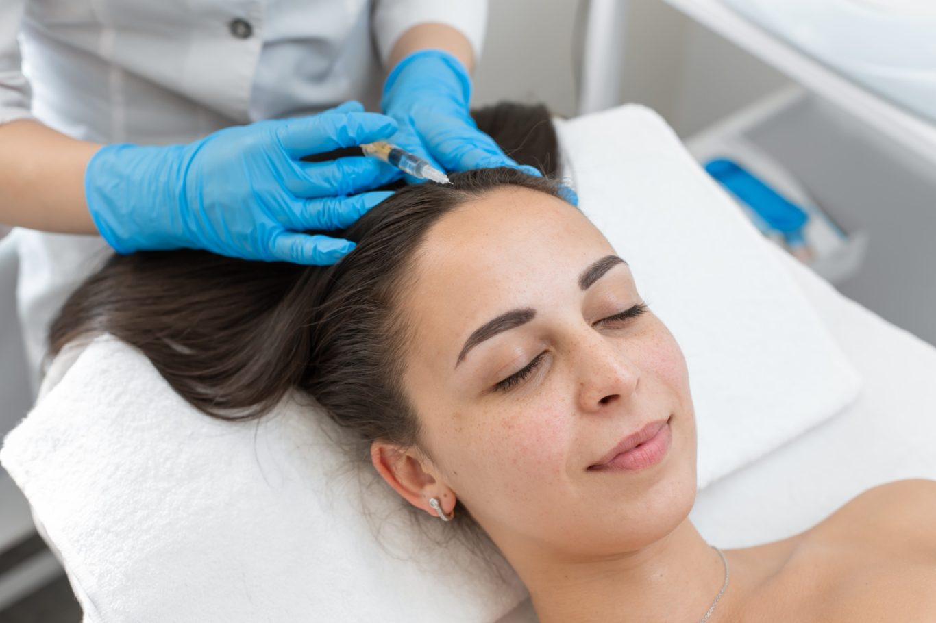 A woman receiving a facial treatment while lying on a treatment bed.